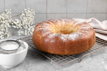 Freshly baked sponge cake with powdered sugar and flowers on grey table, closeup