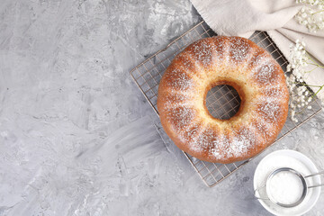 Freshly baked sponge cake with powdered sugar and flowers on grey table, top view. Space for text