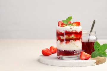 Tasty trifle dessert. Strawberries, sponge cake and whipped cream in glass on beige table, space...