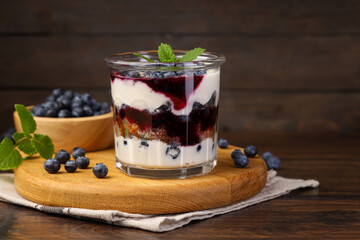 Tasty trifle dessert. Blueberries, sponge cake and whipped cream in glass on wooden table, space for text