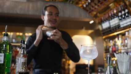 Asian smart bartender shaking mixed cocktail preparing to serve at luxurious counter preparation, making special drink looking at camera fronted view. Special refresh drink nightlife luxury. Vinosity.
