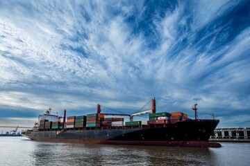 Large container ship with cargo freight in port with dramatic sky behind it
