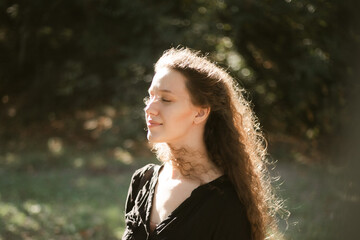 Girl in nature in the park. Curly girl in a linen dress. Sunny day and beautiful sunlight. Warm photos of a girl enjoying nature in a good mood. Walking alone with yourself and the beauty of nature.