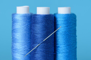 Row of blue thread spools with needle aligned background with copy space for text close-up flat lay top view