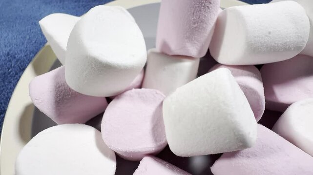 Macro closeup slow dolly shot of a pile of soft pieces of barrel shaped, pink and white marshmallow confectionery candy, on a plate.