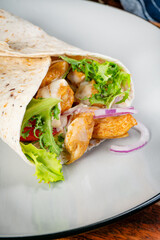 Wholegrain tortilla wraps with vegetables and chicken on a plate.
