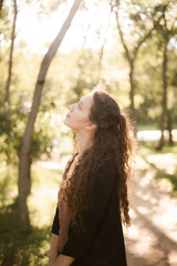 Girl in nature in the park. Curly girl in a linen dress. Sunny day and beautiful sunlight. Warm photos of a girl enjoying nature in a good mood. Walking alone with yourself and the beauty of nature.