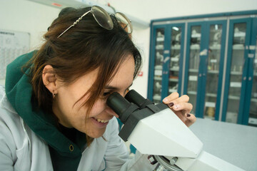 Young scientist woman in laboratory looking in a microscope, using lab coat. Lab background of medicine, chemistry, biology or physics 