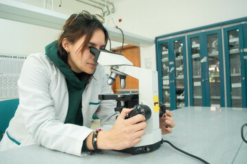 Young scientist woman in laboratory looking in a microscope, using lab coat. Lab background of medicine, chemistry, biology or physics 
