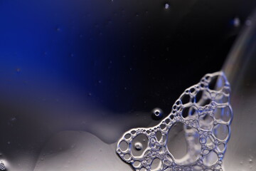 Transparent liquid, bubbles of thick liquid, silver reflection on dark background, gray surface