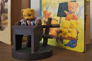 A toy bear standing by a wooden bench. We also see children's literature.