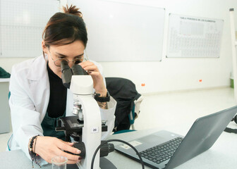 Young scientist woman in laboratory looking in a microscope, using lab coat. Lab background of medicine, chemistry, biology or physics 