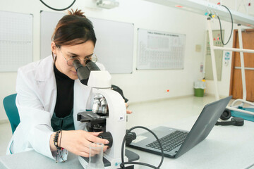 Young scientist woman in laboratory looking in a microscope, using lab coat. Lab background of medicine, chemistry, biology or physics 