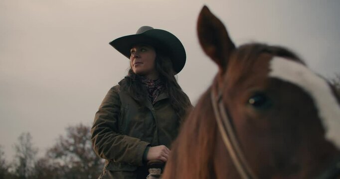 Panning Close Up of Horse's Face and Cowgirl Woman Wearing Cowboy Hat Looking Off Into Distance With Sunset Cloudy Sky