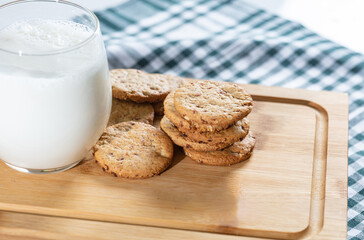 A delightful display of freshly baked  cookies arranged on a wooden cutting board with  a cup of milk 