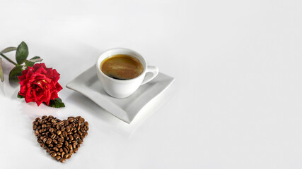 A cup of black coffee, a heart made of beans and a red rose on a white background.