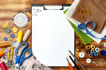 Colorful sewing supplies arranged around a blank clipboard on a wooden table
