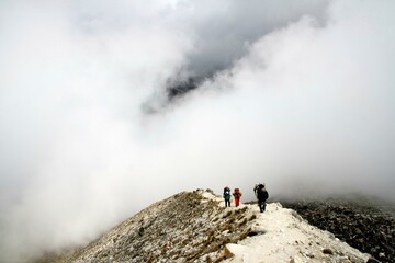 Climbers ascend a rocky path on Huayna Potosí, Bolivia, surrounded by dense clouds, highlighting...