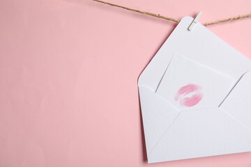 White envelope and card with lip print hanging on twine against pink background, space for text....