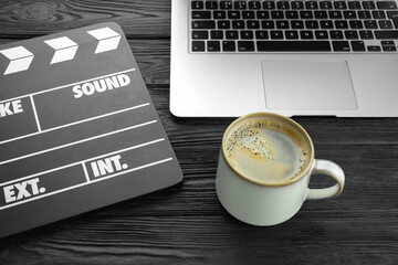 Movie clapper, laptop and cup of coffee on black wooden table, closeup