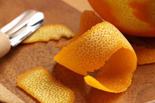 Fresh orange peel, channel knife and fruit on wooden table, closeup