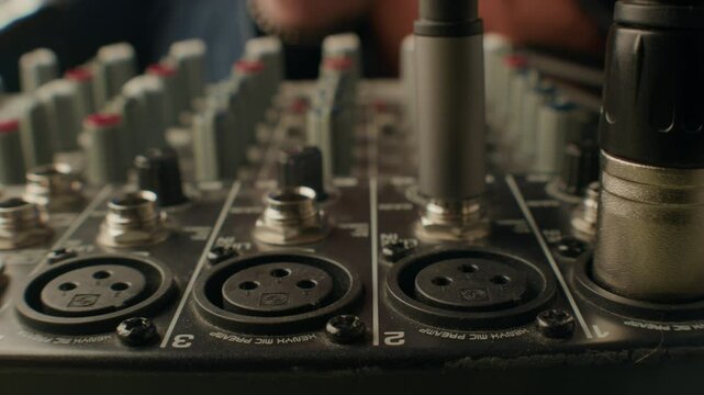 Close up shot of unrecognizable hand connecting audio cables to mixing console in recording studio