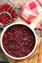 Tasty cranberry sauce in saucepan, berries and cinnamon sticks on wooden table, flat lay
