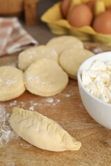 Making pirozhki (stuffed pastry pies). Pieces of dough with cottage cheese on wooden table, closeup