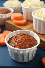 Delicious carrot muffins and fresh vegetables on blue wooden table, closeup