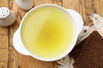 Tasty chicken bouillon in bowl and bread on wooden table, top view
