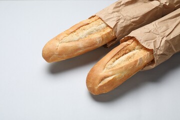 Paper bags with fresh baguettes on white background, closeup. Space for text