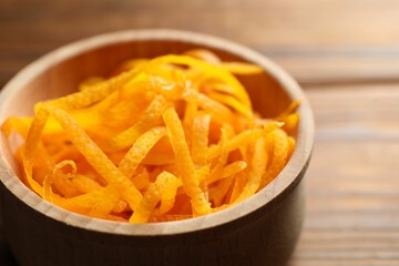 Fresh orange zest in bowl on wooden table, closeup