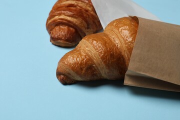 Paper bags with fresh croissants on light blue background, closeup. Space for text