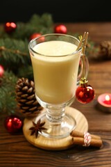 Tasty Christmas cocktail (eggnog) in glass, festive decor and burning candle on wooden table, closeup