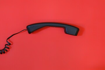 black telephone receiver isolated on red background.