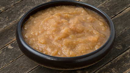 Homemade pureed apple sauce in a bowl on a rustic wooden background.