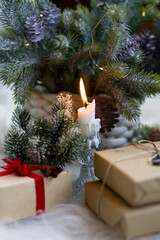 A craft gift box tied with a red bow stands under the Christmas tree. Fluffy branches of a fir tree, New Year