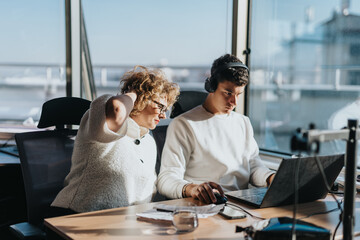 Two business employees collaborating in a bright, modern office. The sunlit room emphasizes focus...
