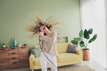 Joyful young woman singing and enjoying music at home in casual style during daylight