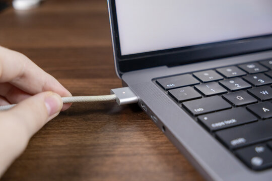 MagSafe charging cable connection to a laptop with LED light indicator glowing on a wooden desk surface