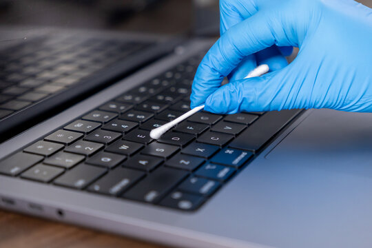 cleaning laptop keyboard with cotton swab and protective gloved hand for hygiene maintenance, close-up view