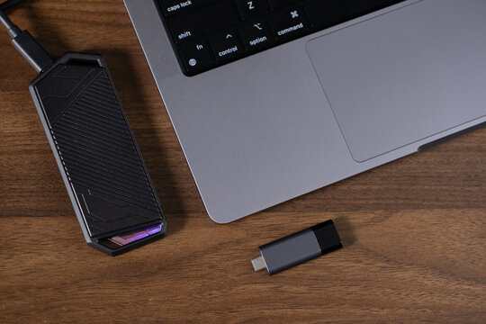 external ssd drive and usb flash drive near laptop on wooden desk, technology and data storage devices