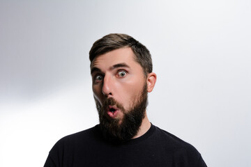 Fototapeta premium Headshot of a surprised man with a beard, his mouth open in astonishment against a plain white backdrop. His expression conveys shock and disbelief.