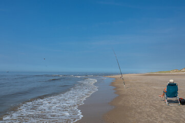 A fisherman sits on the beach with his fishing rod by the sea