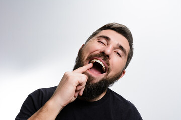 A bearded man in a dark shirt points at his teeth with a smile on his face, set against a plain white background. The image highlights his expression and gesture.