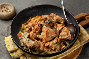 Dark plate with Creamy rabbit and mushrooms stew in a sauce of wine and cream with onion and carrot.
