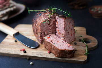 Slices of liver pate rest on a rustic wooden cutting board, paired with spices and a sprig of rosemary.
