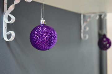 A purple Christmas ball toy hangs alone on a shelf with monograms against a gray wall. High quality...