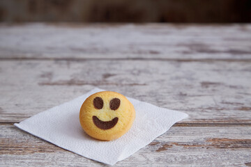 A smiley cookie lying on a white paper napkin on a wooden table, close-up, good news, good mood.