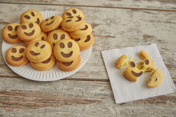 Yellow cookies in the shape of smiling emojis are on a plate, while one broken cookie lies separately on a napkin, close-up, good and bad mood, sadness and joy side by side.